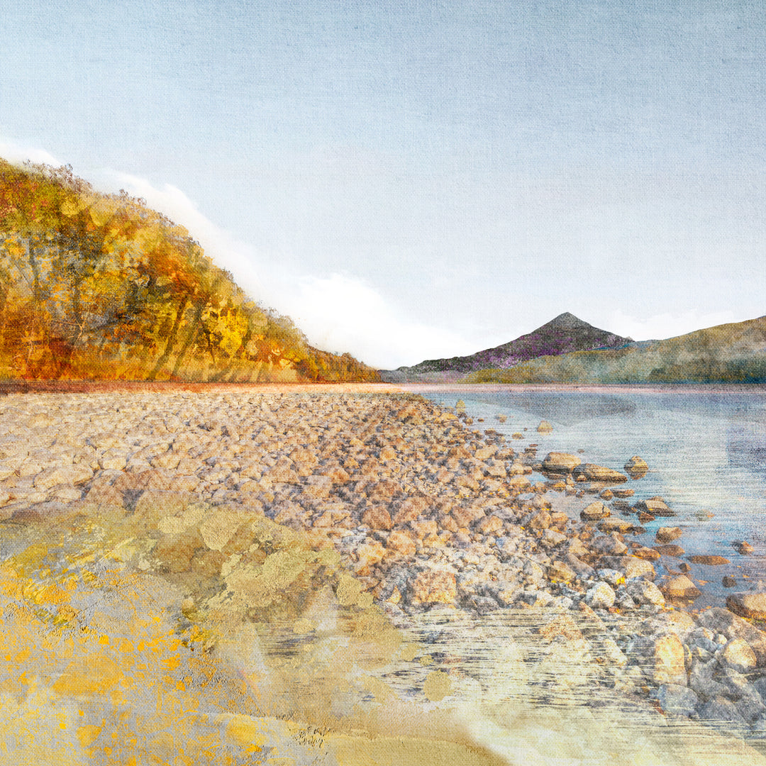 Scottish mountain Schiehallion in the distance, viewed from Loch Rannoch. The trees on the left are a golden colour and in the foreground is a rocky loch shore.