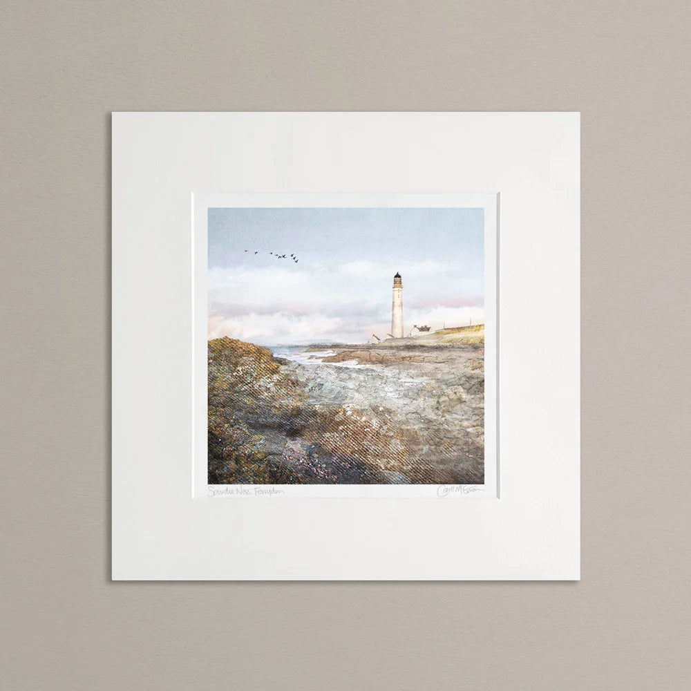 mounted print of Scurdie Ness lighthouse picture with a light blue & pink sky, gees flying in the distance and textured brown rocks in the foreground. The mount is placed on a beige coloured wall