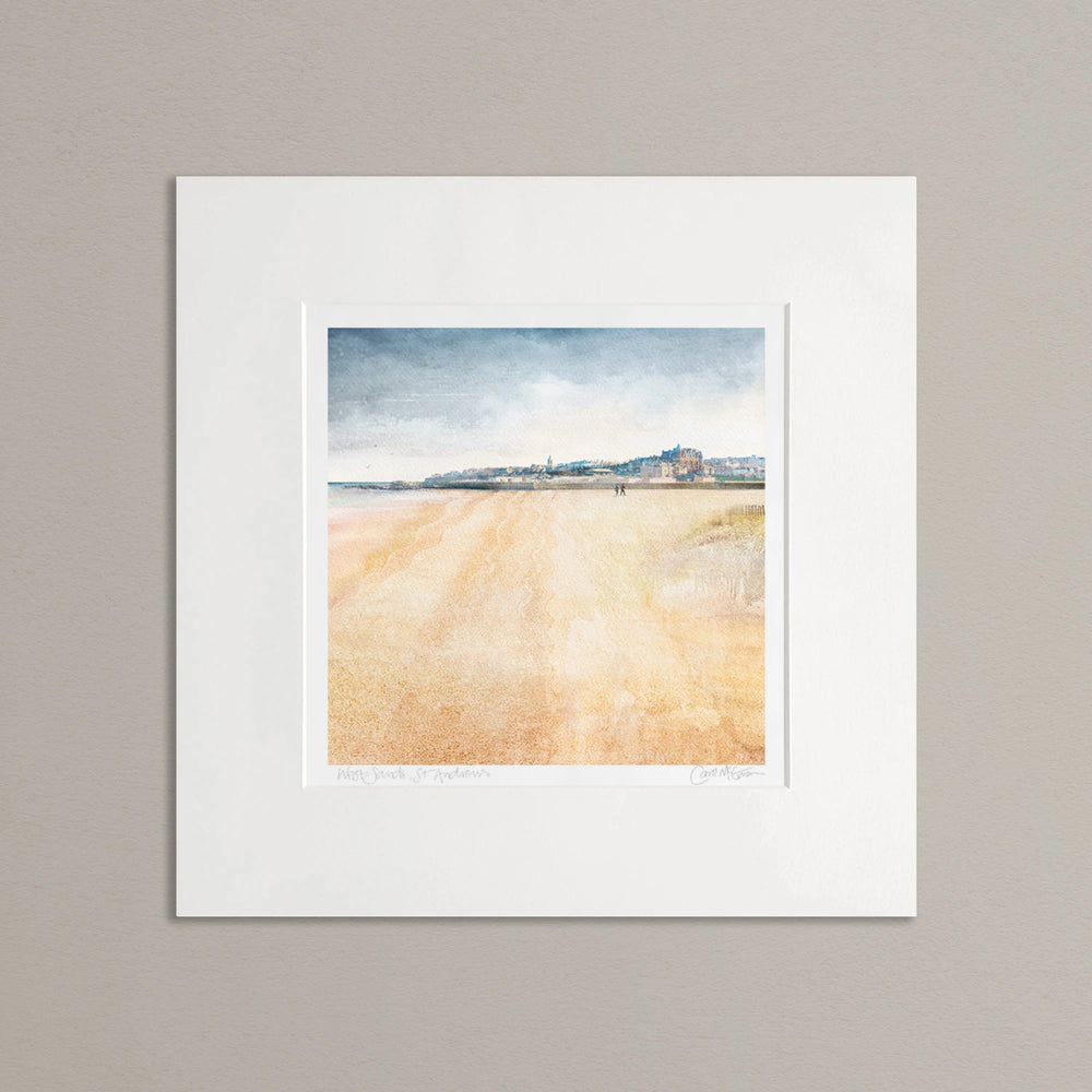 A mounted art print of West Sands, St Andrews, against a neutral grey background. The top 1/3 of the picture is the town shown as a view from the beach. The bottom part of the image is the beach. The sky is a muted blue grey. Overall the artwork is calming. There are 2 people walking in the distance on the beach